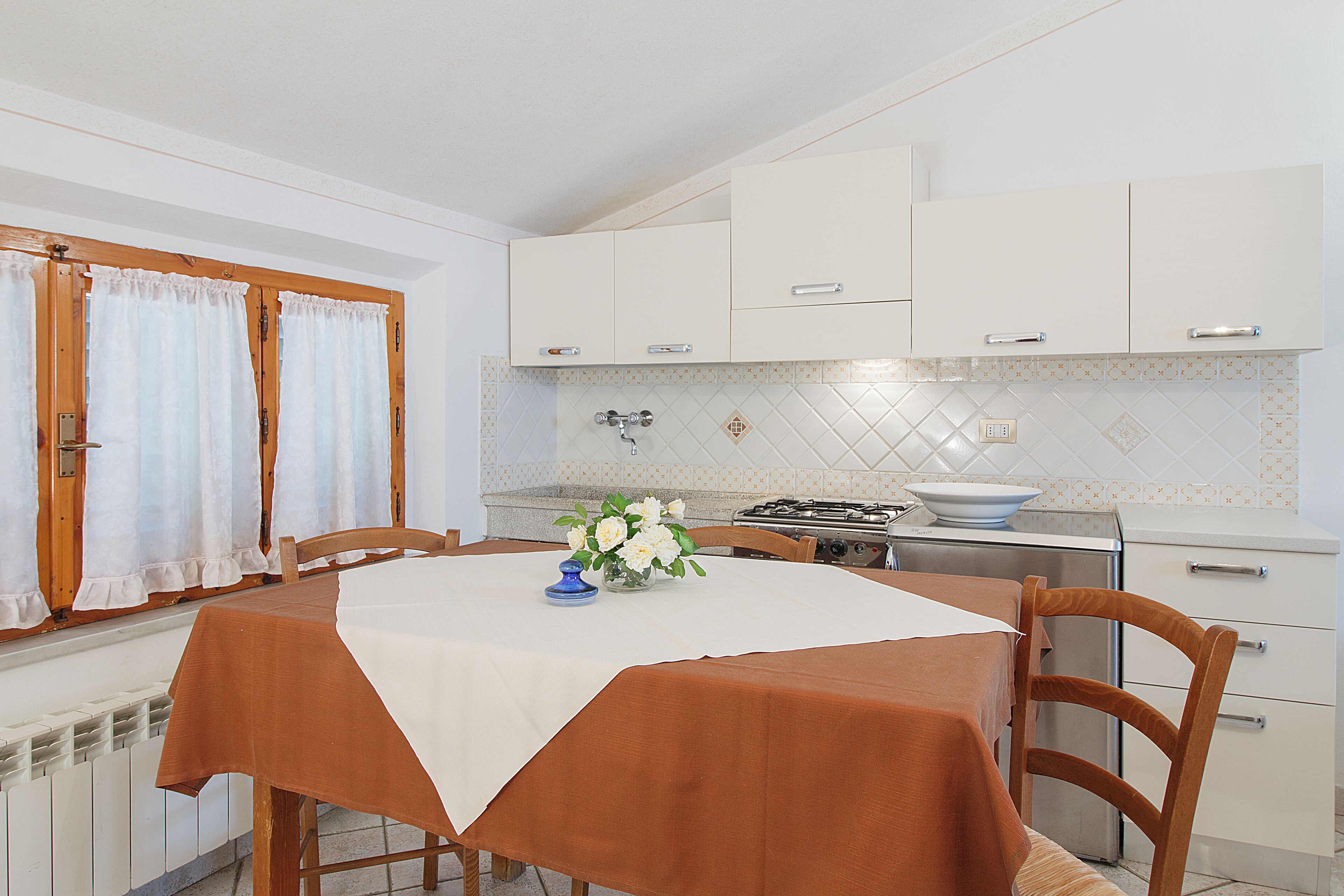 A kitchen with white cabinets, a stove, and a dining table with a brown tablecloth.