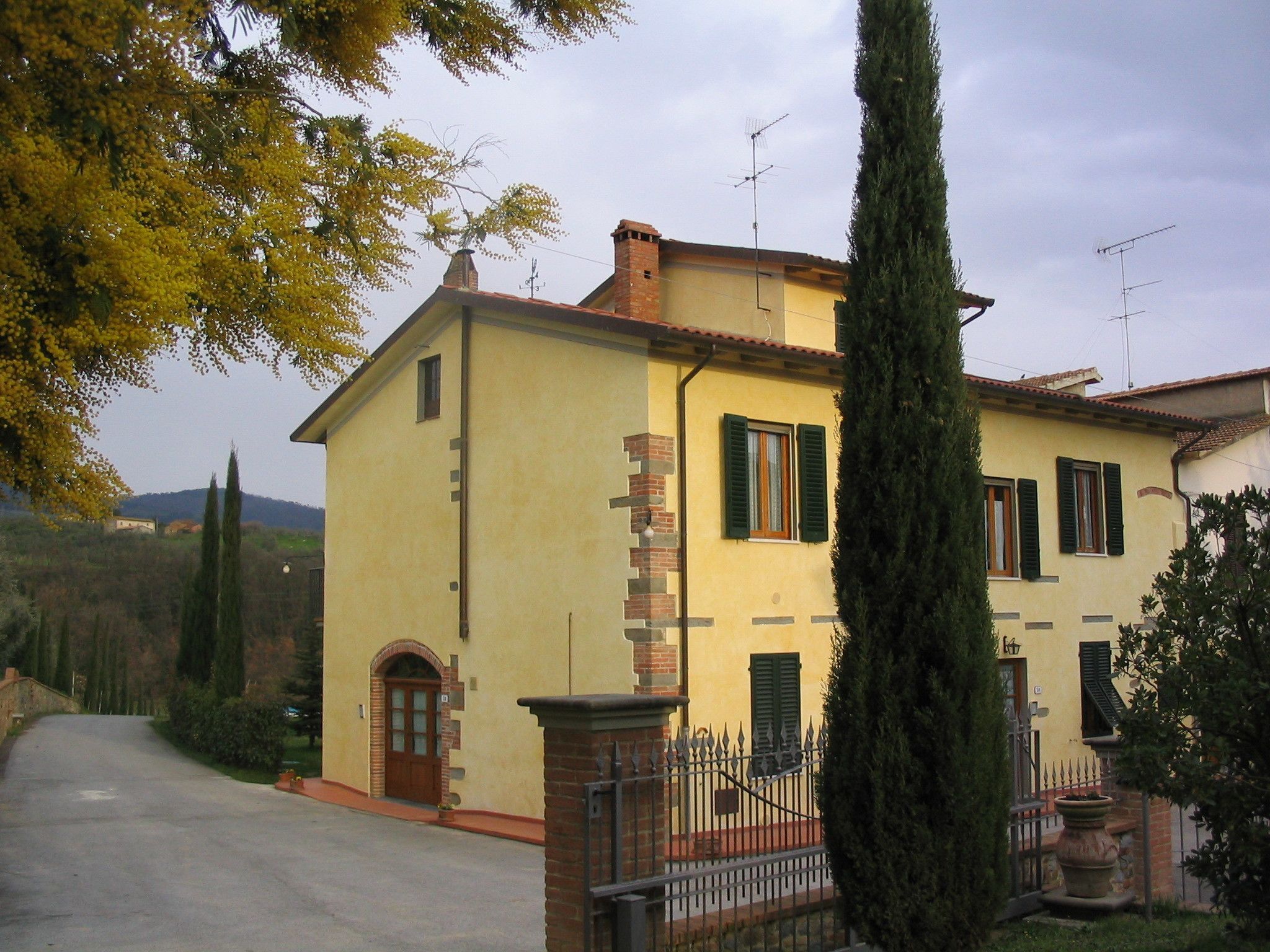 A two-story house with a yellow facade, green shutters, and a brick chimney.