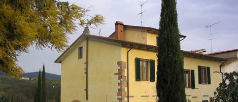 A two-story house with a yellow facade, green shutters, and a brick chimney.