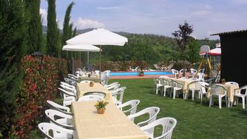 An outdoor dining area with white plastic chairs and tables, a pool, and a scenic hillside view.