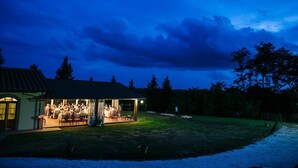 A covered outdoor dining area with tables and chairs, a building with a tiled roof, and a grassy lawn. - Il Piastrino (Vinci)