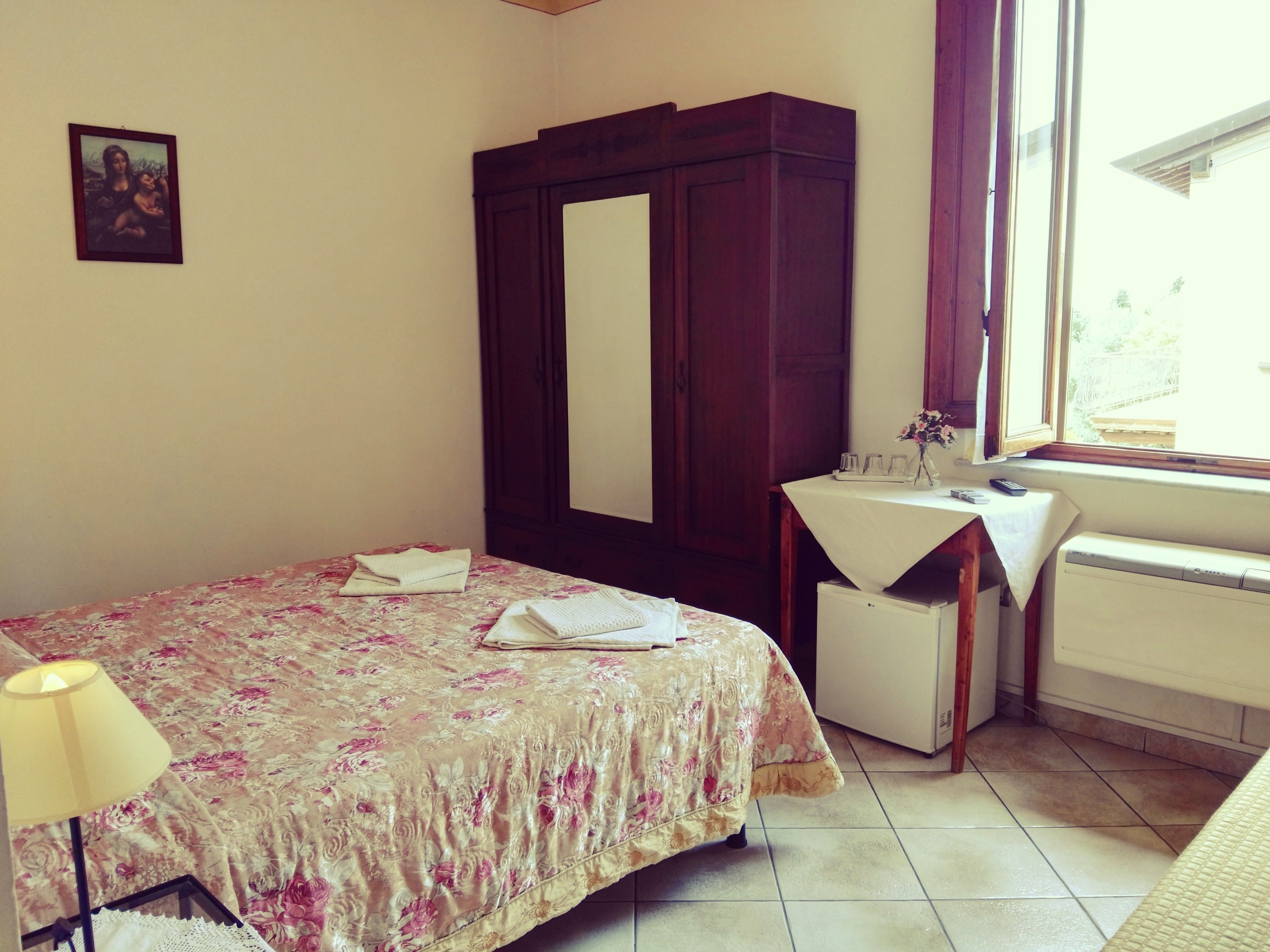 Un dormitorio con cama, cómoda, mesita de noche con lámpara, ventana y radiador.