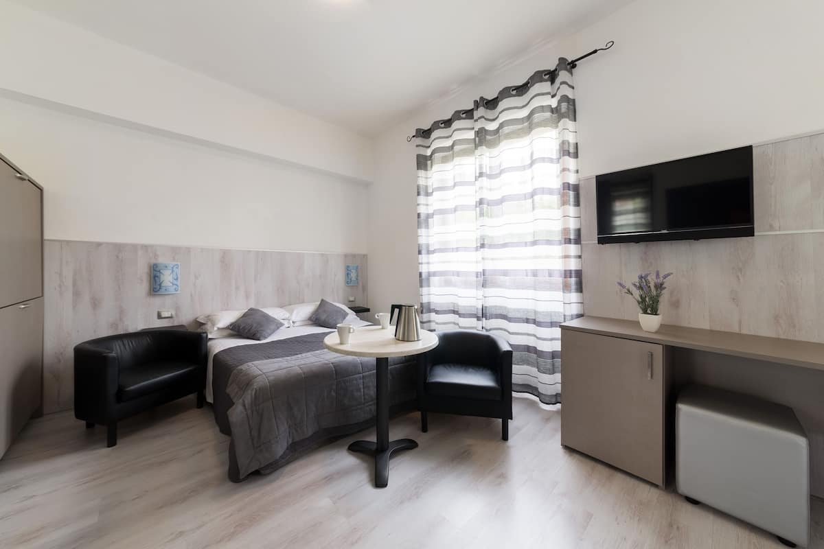 Un dormitorio moderno con cama, mesitas de noche, un escritorio pequeño y un televisor montado en la pared.