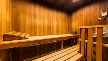 A sauna with wooden walls and benches. There is a shelf with a pot and a hanging scale.