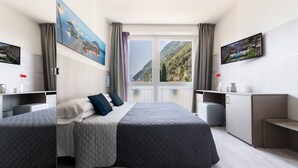 A modern hotel room with two beds, a TV, a painting, and a view of mountains.