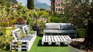 A rooftop garden with a white outdoor seating area, potted plants, and a mountain view.