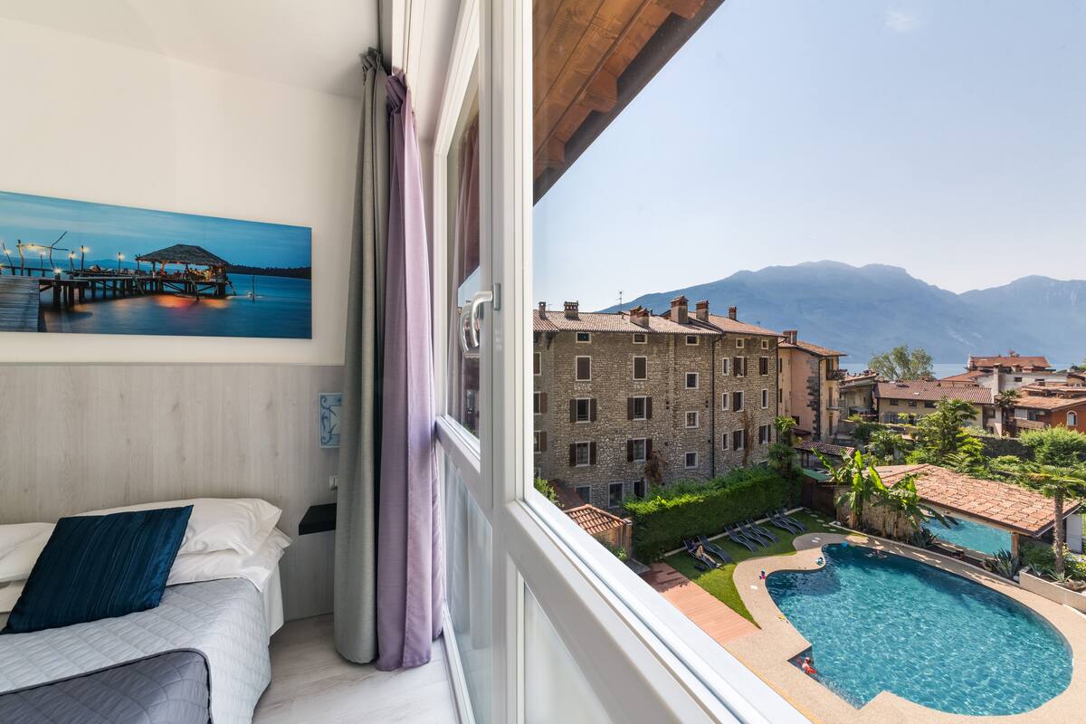 Habitación de hotel con cama, un cuadro de un muelle, vista a una piscina y edificios.