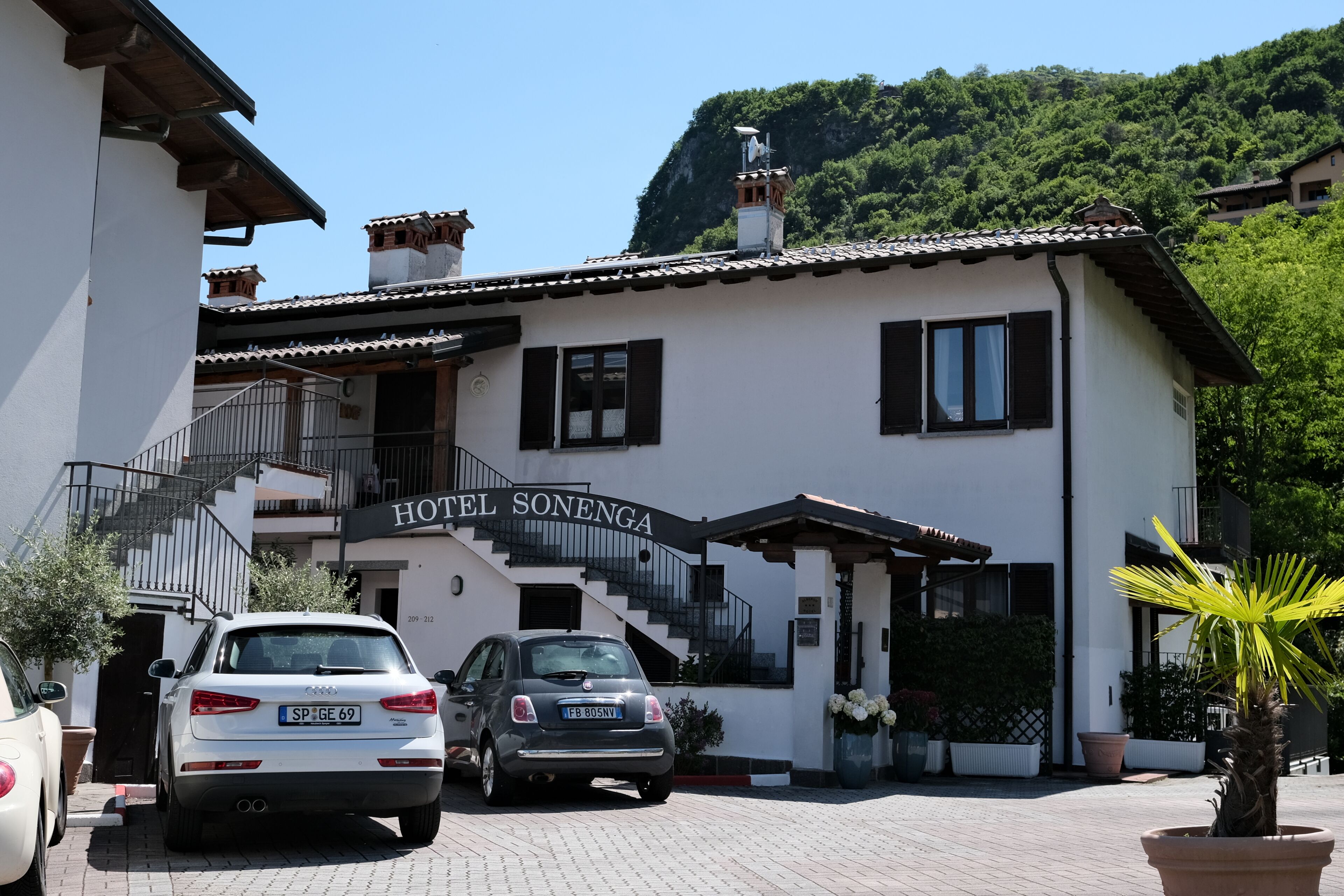 A hotel named 'HOTEL SONENGA' with a staircase leading to the entrance, parked cars, and a mountainous backdrop.