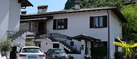 A hotel named 'HOTEL SONENGA' with a staircase leading to the entrance, parked cars, and a mountainous backdrop.
