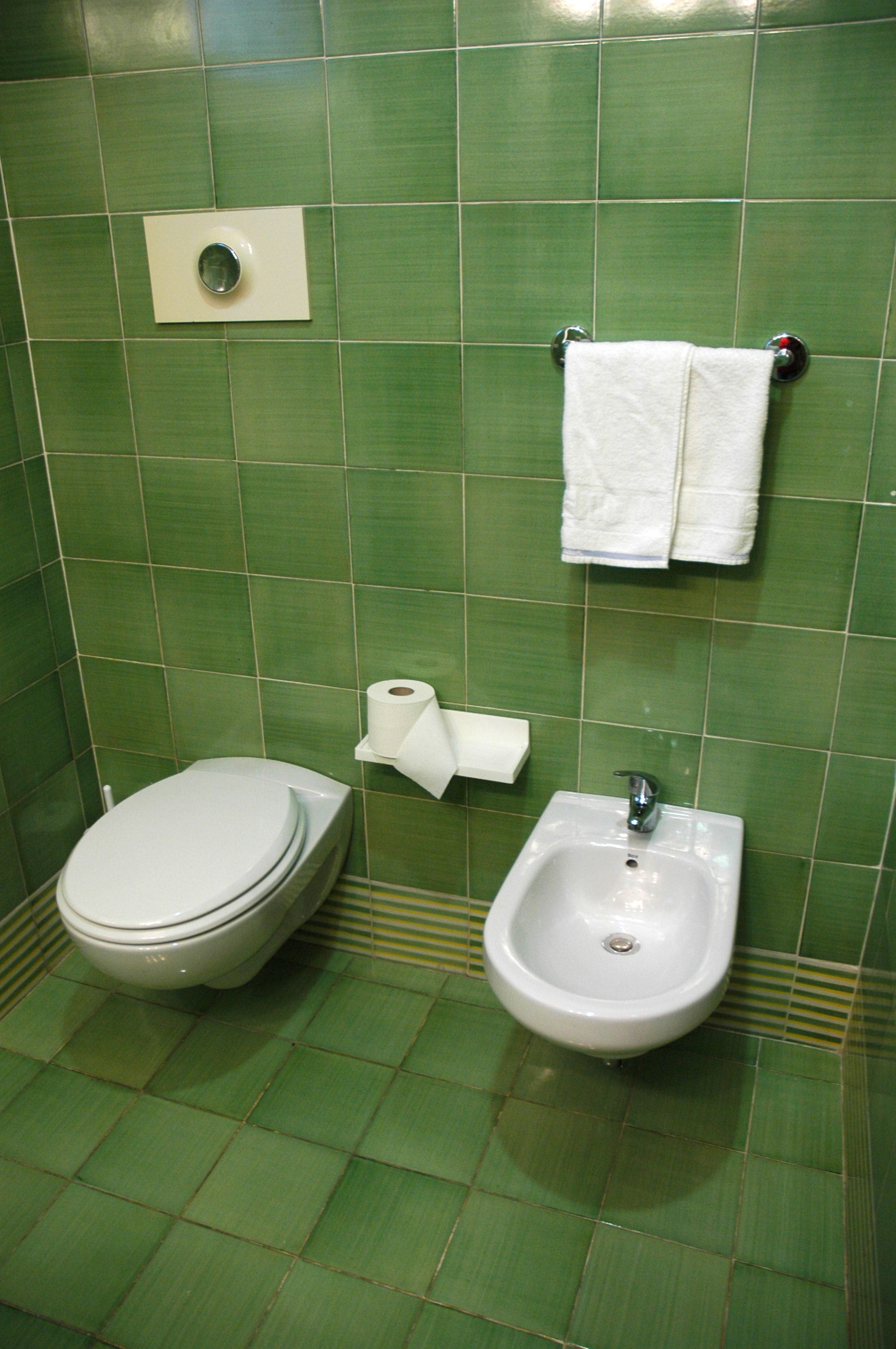 Ein Badezimmer mit grünen Fliesen, einer weißen Toilette, einem Bidet und einem Handtuchhalter mit einem weißen Handtuch.