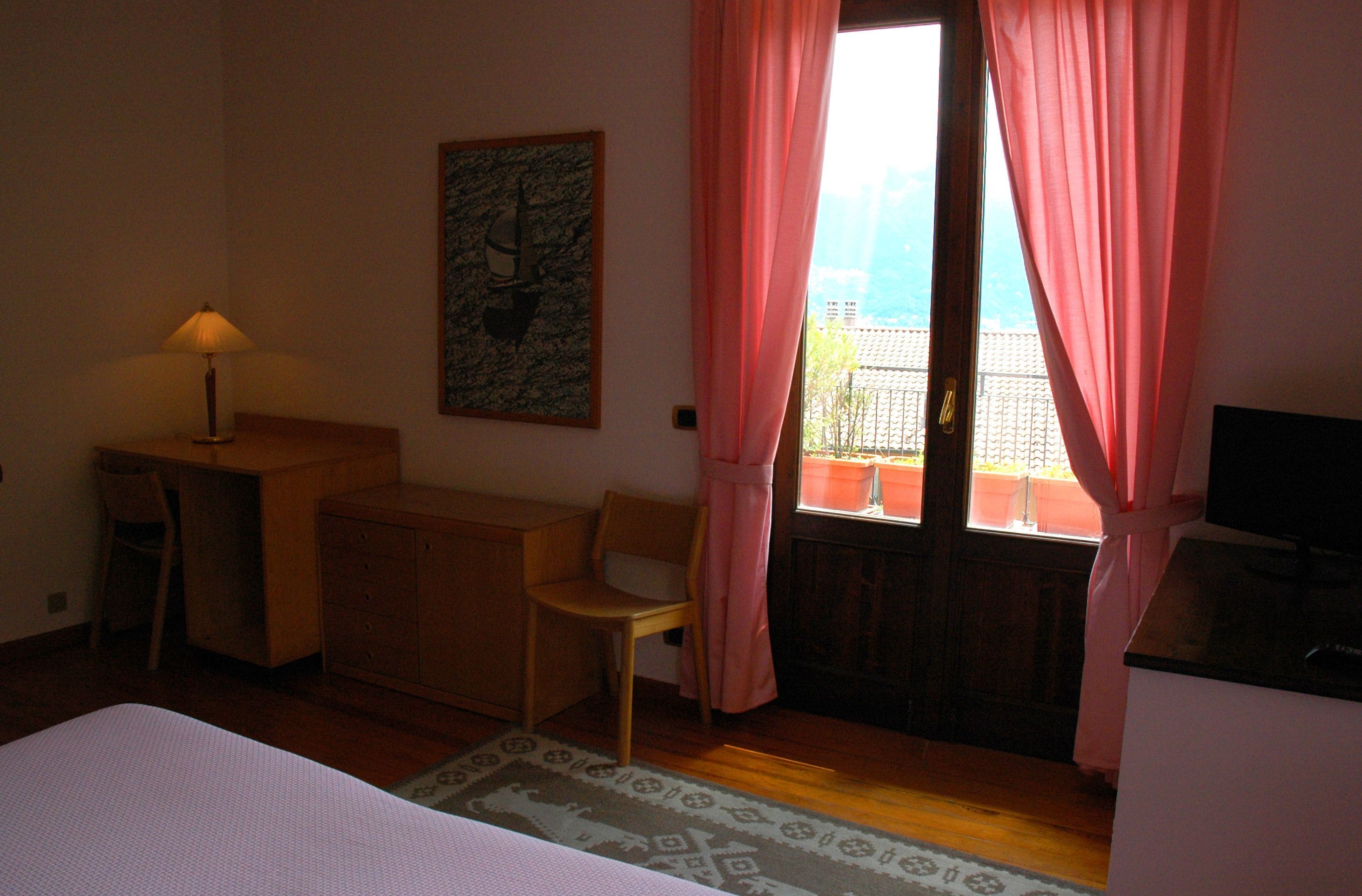 A hotel room with a bed, a desk, a chair, a television, and a window with curtains.