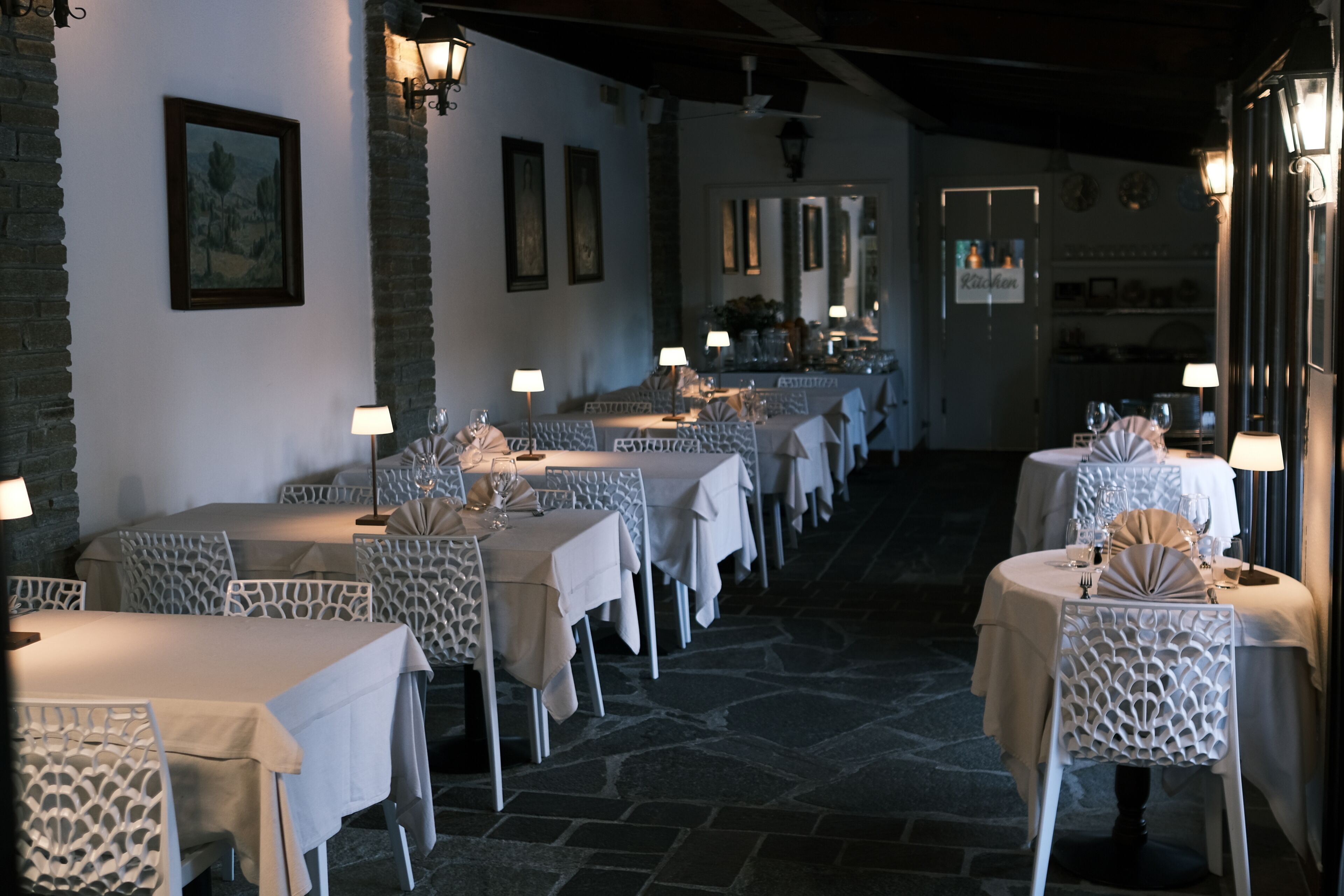 A restaurant with white tablecloths, white chairs, and table lamps.
