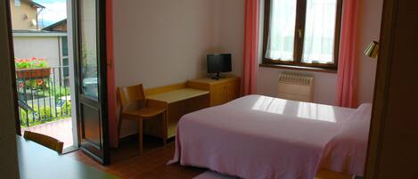 Une chambre à coucher comprenant un lit, un bureau, une chaise, un téléviseur et une fenêtre avec des rideaux.