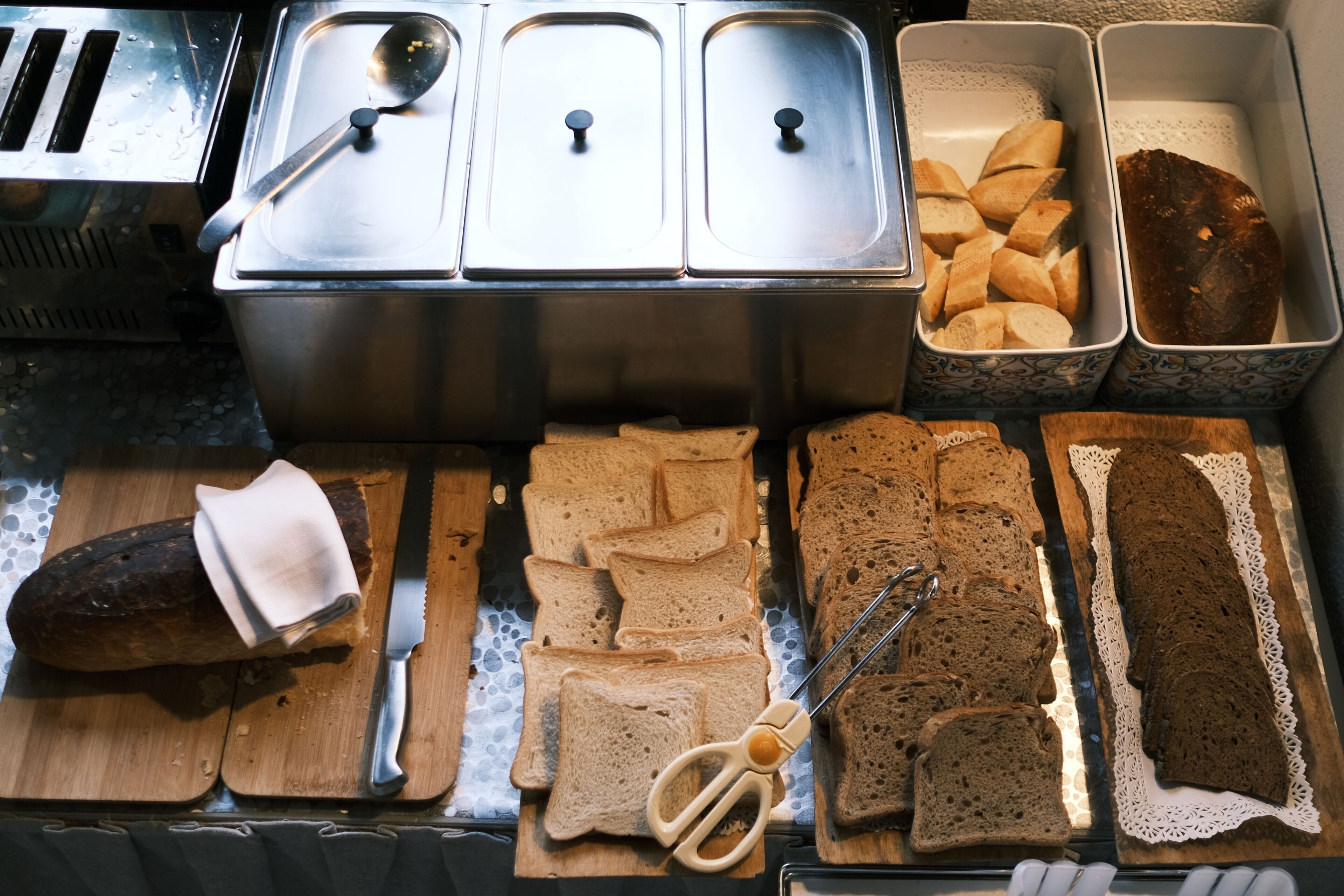 A buffet with various breads and a loaf of bread on a cutting board.