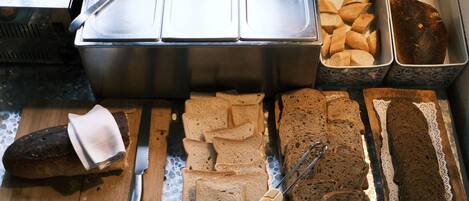 A buffet with various breads and a loaf of bread on a cutting board.