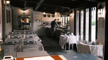 Een restaurant met gedekte tafels, een kok in de weer met eten, en uitzicht op de straat door grote ramen.