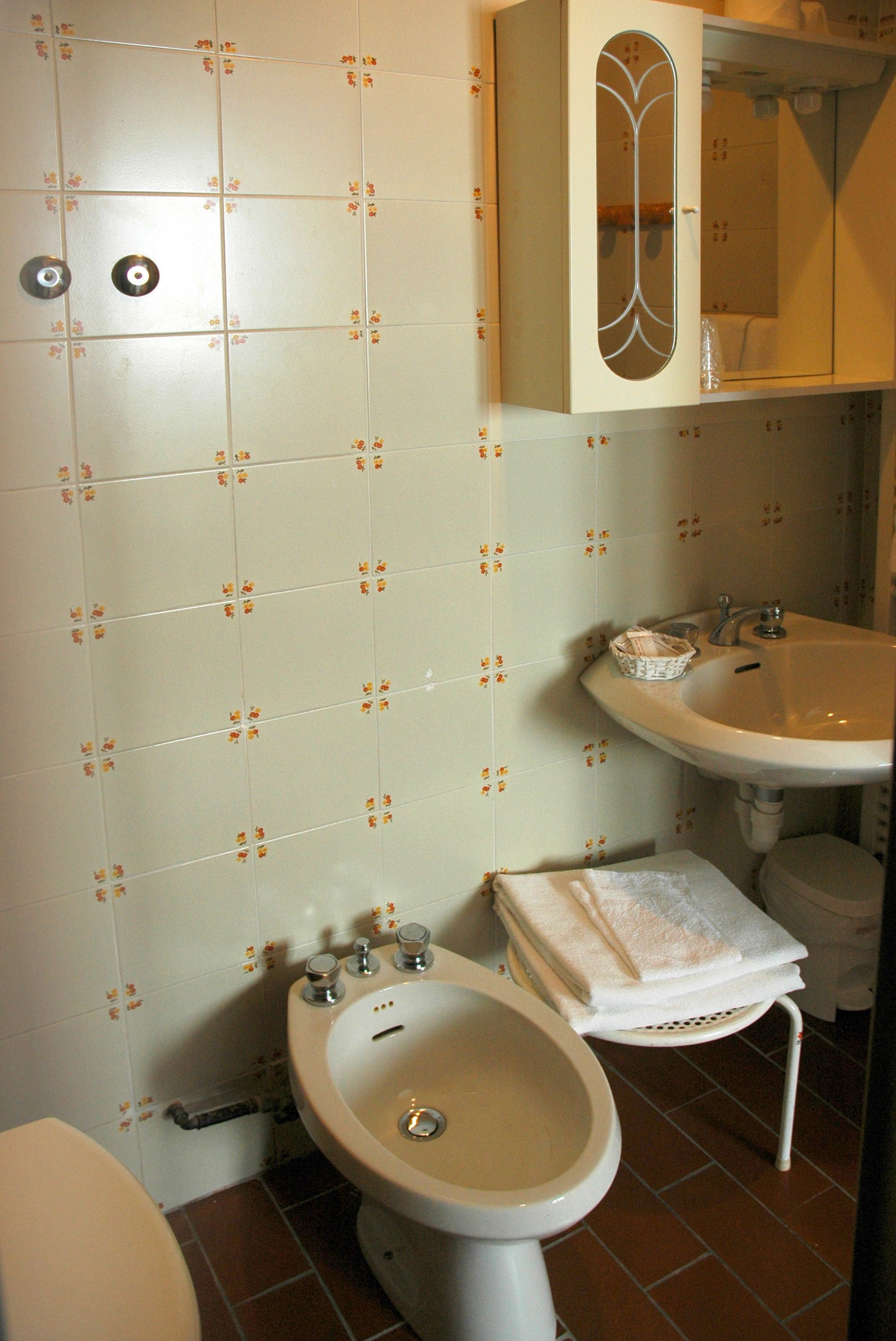 A bathroom with a toilet, bidet, sink, and a cabinet with a mirror.