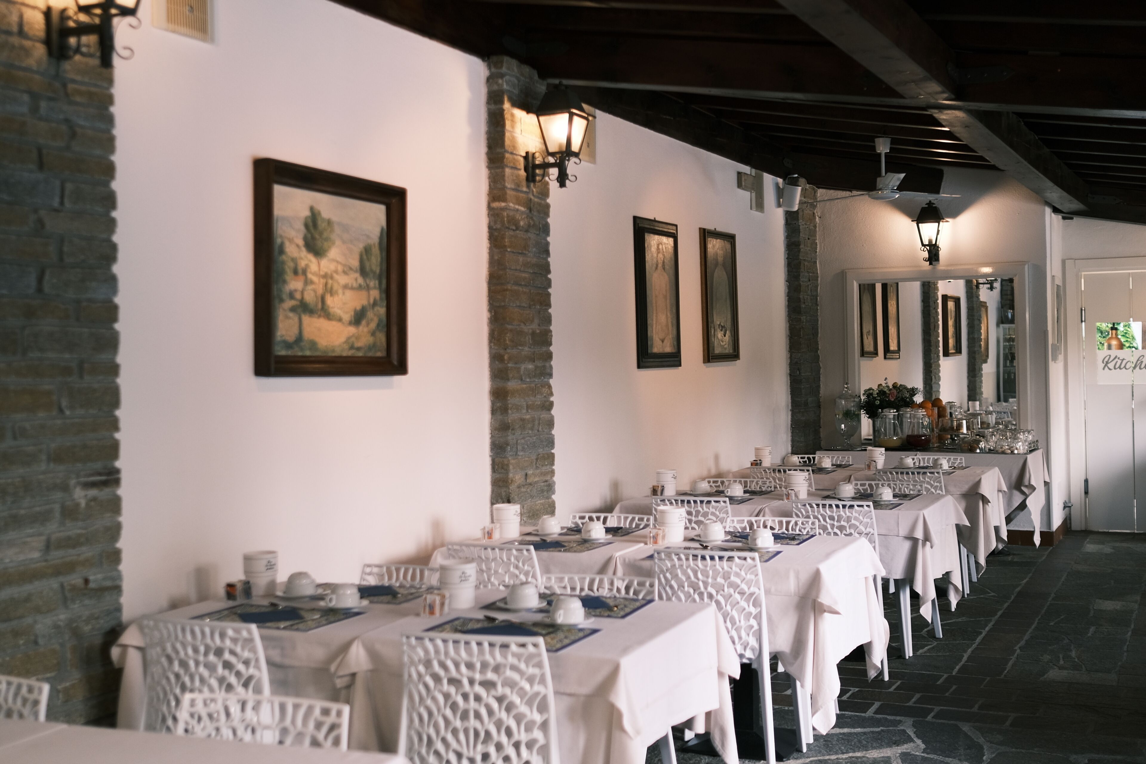 A restaurant with long tables, white chairs, and framed artwork on the walls.
