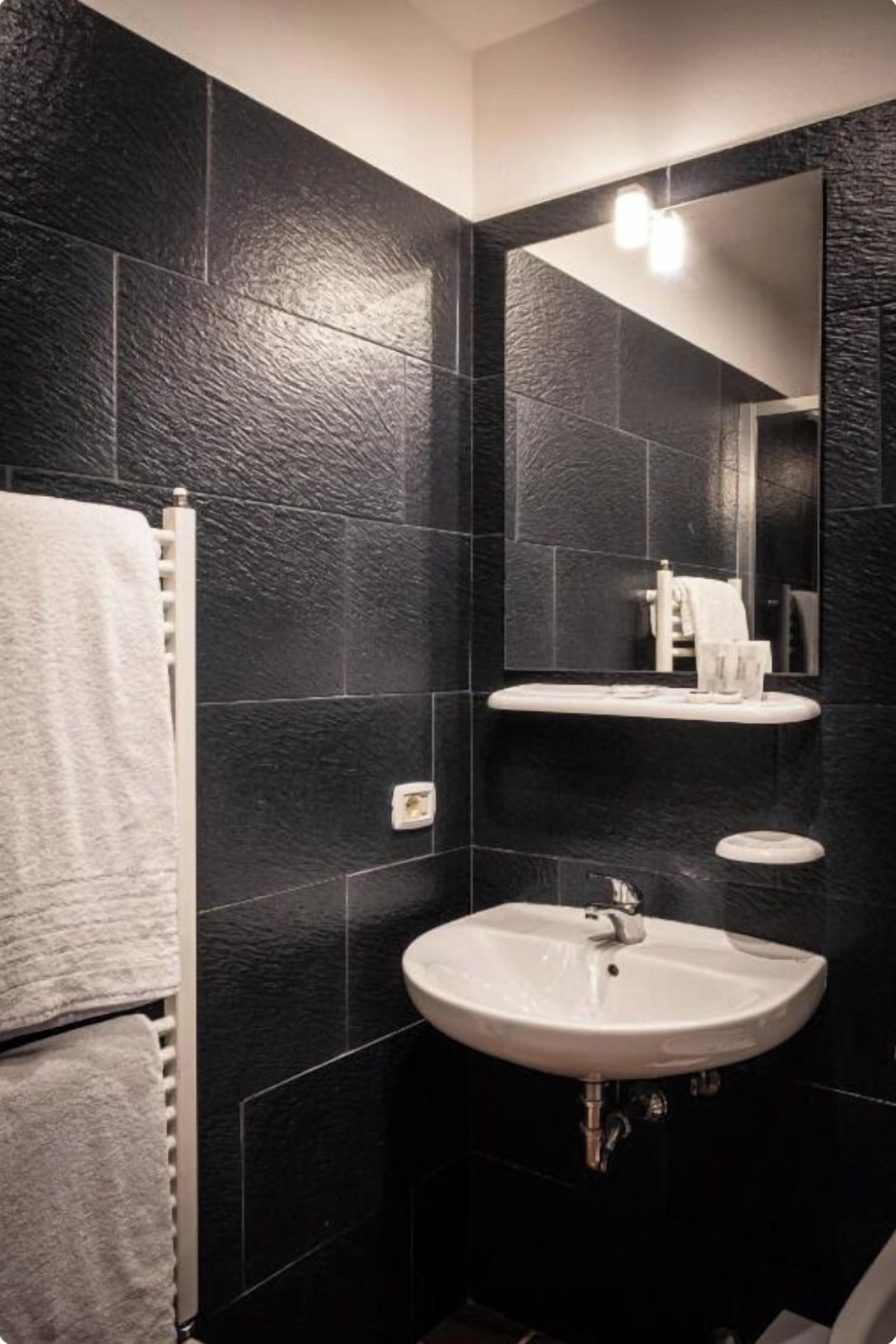 A modern bathroom with black tiled walls, a white sink, and a mirror.