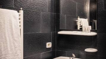 A modern bathroom with black tiled walls, a white sink, and a mirror.