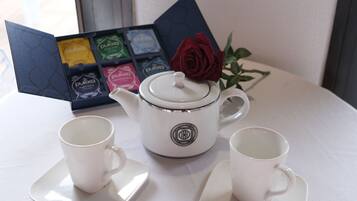 Une théière blanche avec un couvercle, deux tasses blanches sur des soucoupes et un ensemble de boîtes à thé décorées d’une rose, le tout posé sur la table.