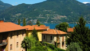 A coastal village with terracotta-roofed buildings, lush greenery, and a mountainous backdrop. - Hotel Sonenga (Menaggio)