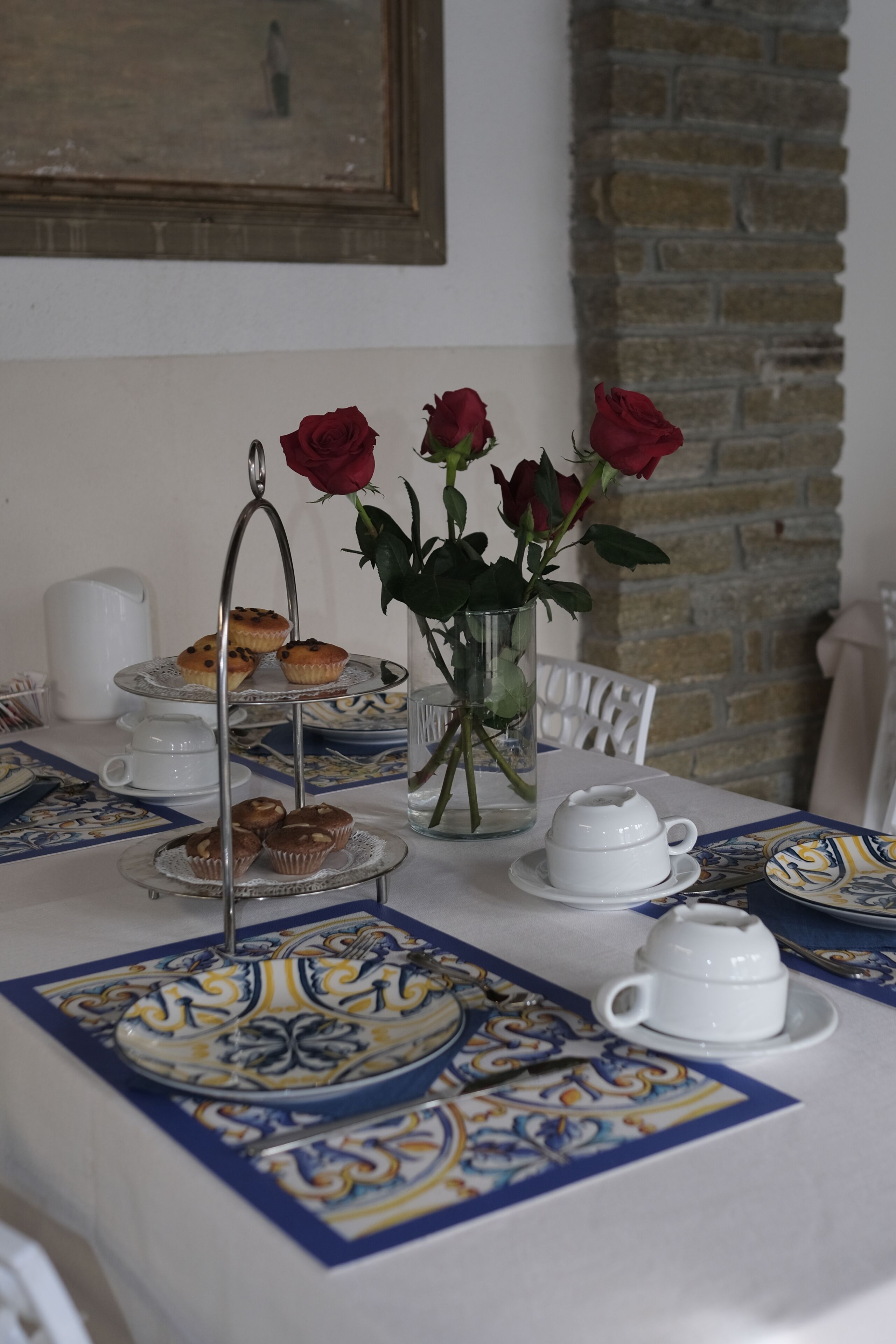 A table set with a tiered stand holding muffins, a teapot, and a vase with roses.