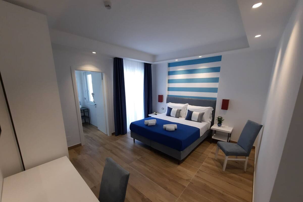 Una habitación de hotel moderna con una cama grande, una mesita de noche, una silla y un escritorio.