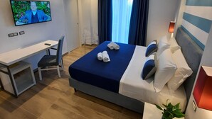 Una habitación de hotel moderna con cama, escritorio, silla, televisor y una planta en maceta.