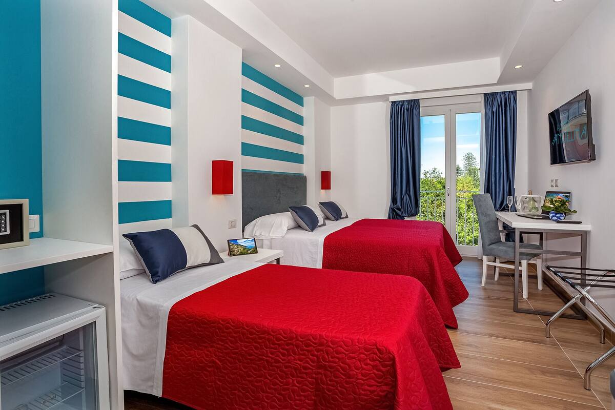 Habitación de hotel con dos camas, un escritorio y un balcón con cortinas.