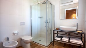 Un baño moderno con ducha envuelta en vidrio, inodoro blanco, bidé, lavamanos con espejo y estante con toallas.