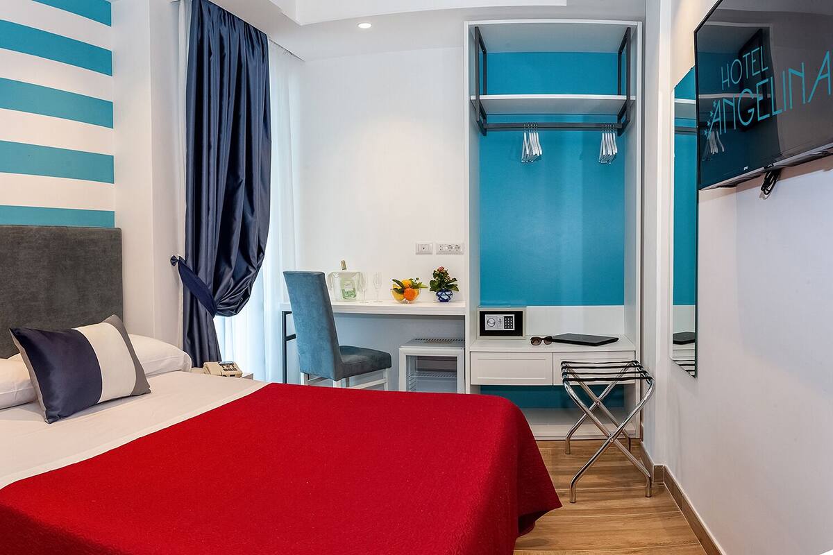 Una habitación de hotel con cama, escritorio, silla, televisor y espejo.