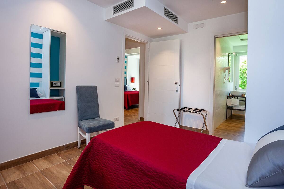 Una habitación de hotel con una cama, una silla, un espejo y un baño visible a través de una puerta abierta.