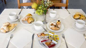 Una mesa de desayuno dispuesta con platos de pasteles, un florero con flores y un bol de fruta.