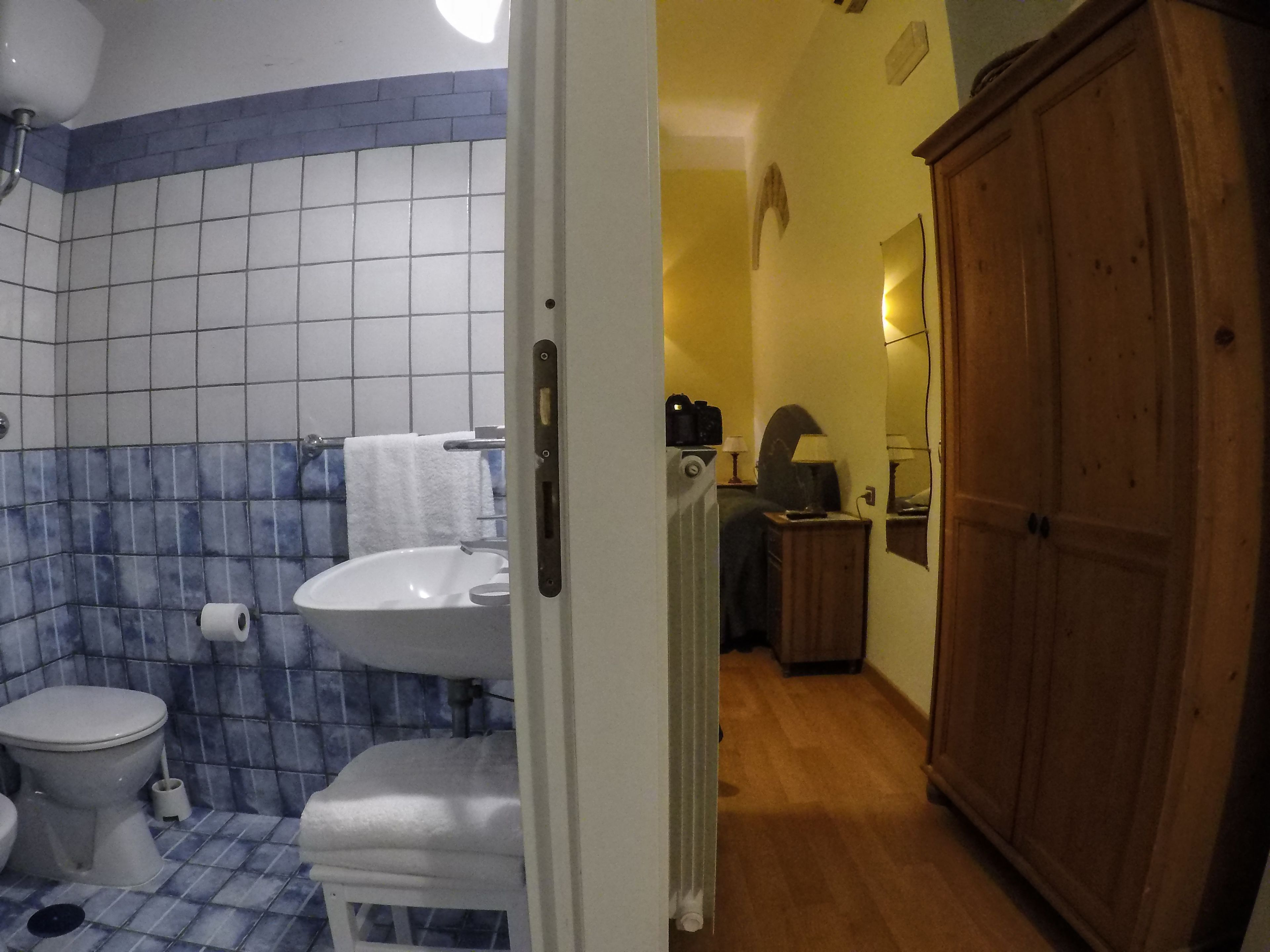 Een badkamer met toilet, wastafel en douche. Er is een houten kastje en een spiegel aan de muur.