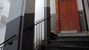 Una escalera con una puerta de madera en la parte superior, barandales metálicos y una pared con un diseño de rayas verticales.