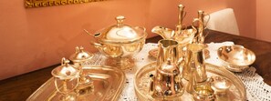Een gedekte tafel met divers zilverwerk en servies, waaronder een theepot, kopjes en borden, geplaatst op een kantdoek.