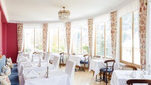 A dining area with tables set for service, large windows with floral curtains, and a chandelier. - Villa Excelsior Hotel Kurhaus (Bad Gastein)