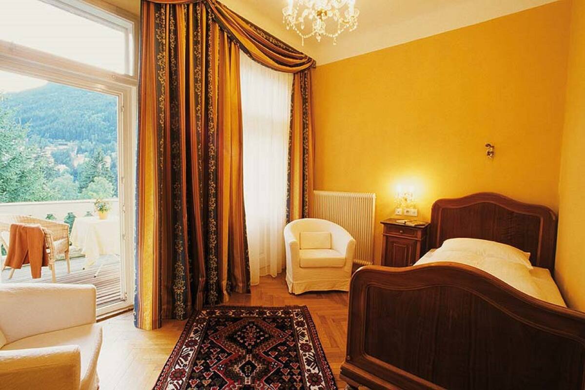 Une chambre avec un lit, une chaise, un radiateur et une vue sur l’extérieur.