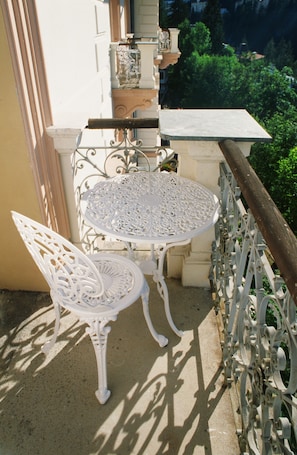 Un balcon avec une table et une chaise en métal blanc, une petite plante en pot et une vue sur la verdure.