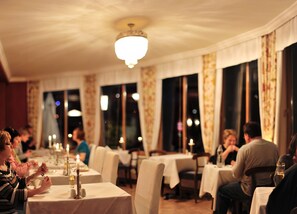 Un restaurant avec des tables dressées, de grandes fenêtres ornées de rideaux et un lustre.