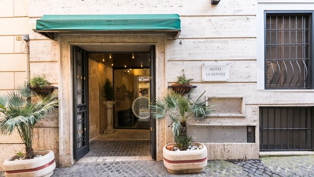 L’entrée d’un hôtel, avec un auvent vert, une enseigne indiquant « HÔTEL LA ROYERE » et des plantes en pot de chaque côté.