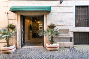 L’entrée d’un hôtel, avec un auvent vert, une enseigne indiquant « HÔTEL LA ROYERE » et des plantes en pot de chaque côté.