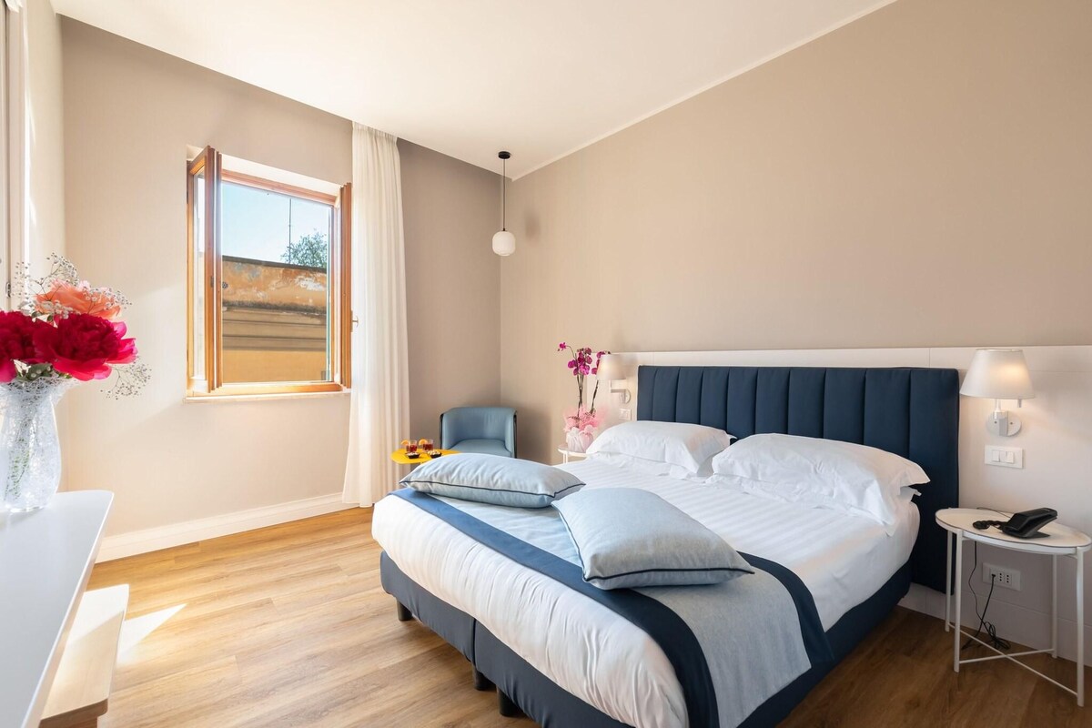 A modern bedroom with a large bed, bedside tables, a desk, and a window with curtains.