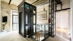 Un intérieur moderne avec des murs en briques apparentes, un ascenseur en verre et un escalier doté de rampes en métal.