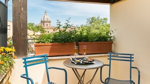 Une petite terrasse extérieure avec deux chaises bleues et une table, une pergola en bois au-dessus, et une vue sur un bâtiment en forme de dôme à l’arrière-plan.