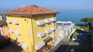 A yellow building with multiple balconies, a red-tiled roof, and a view of the sea.