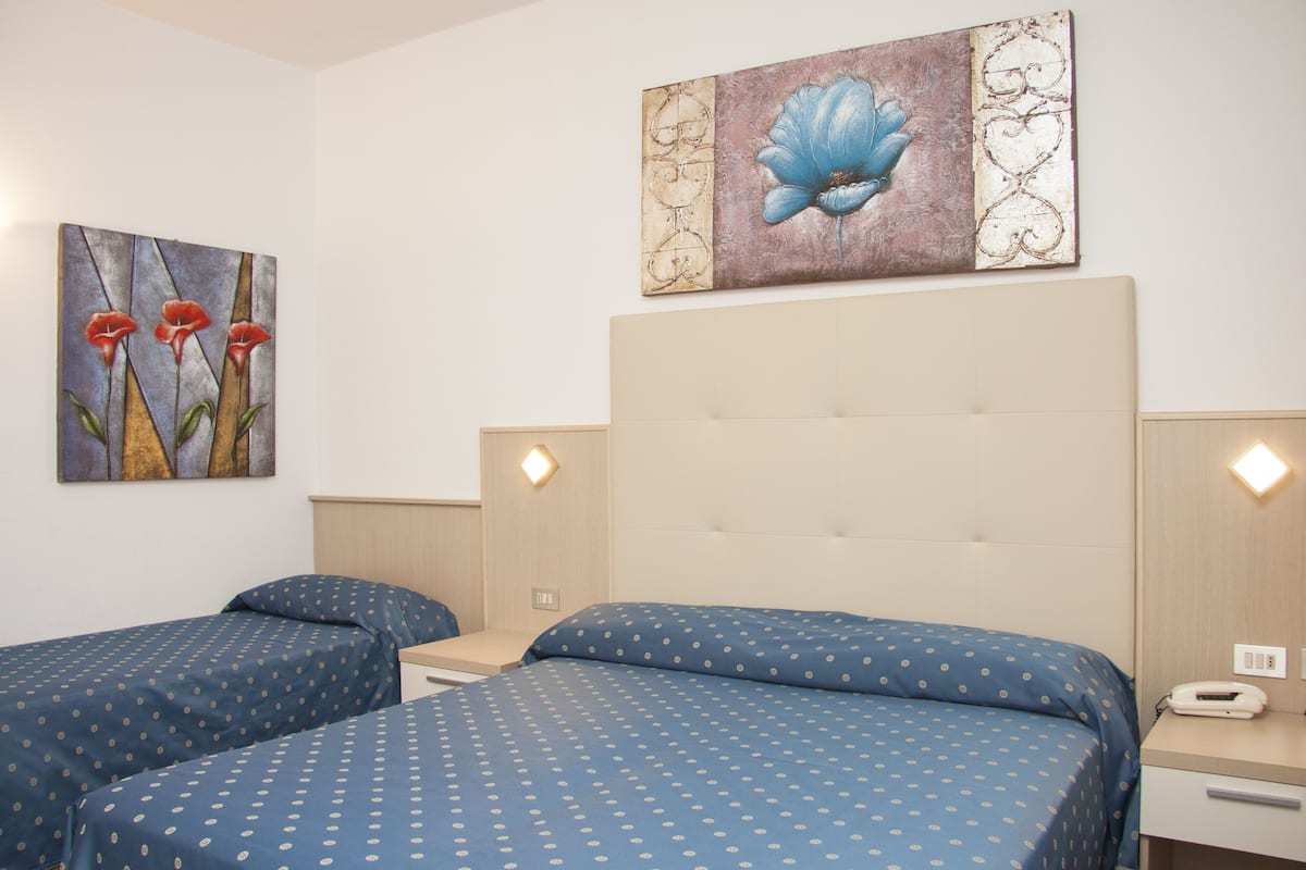 A hotel room with two beds, a headboard, bedside tables, and artwork on the walls.