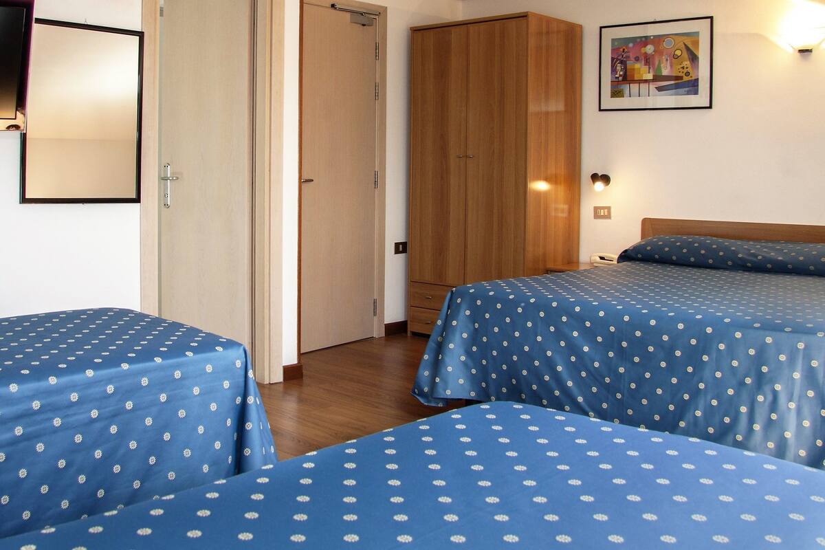 A room with two beds, a wooden wardrobe, a TV, and a wall-mounted light.