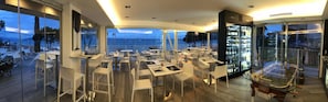 A modern restaurant with a panoramic sea view, glass tables, and a wine refrigerator. - Hotel Ca' Serena (Sirmione)